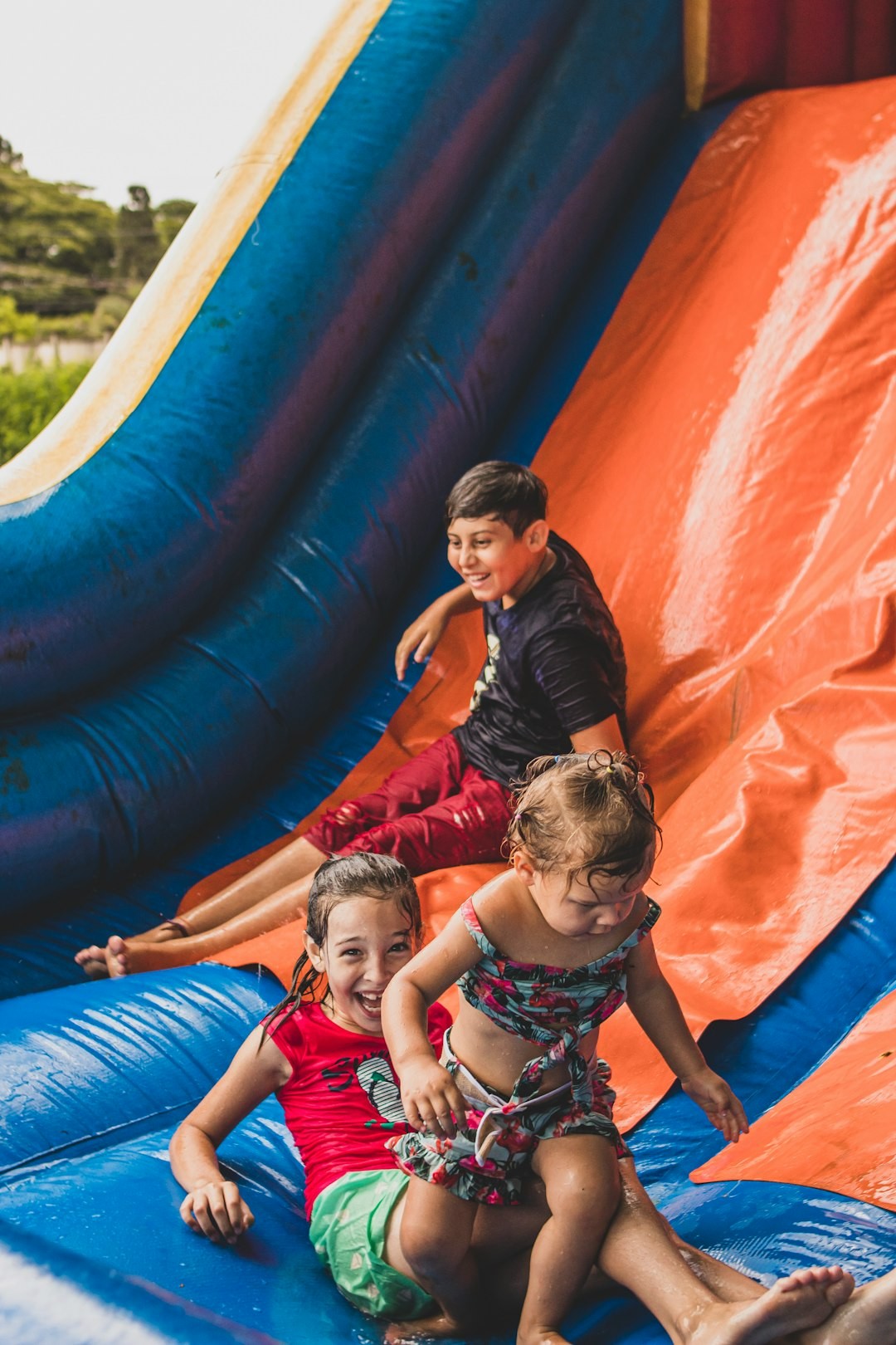 a group of children sitting on top of a blue and orange inflatable slide